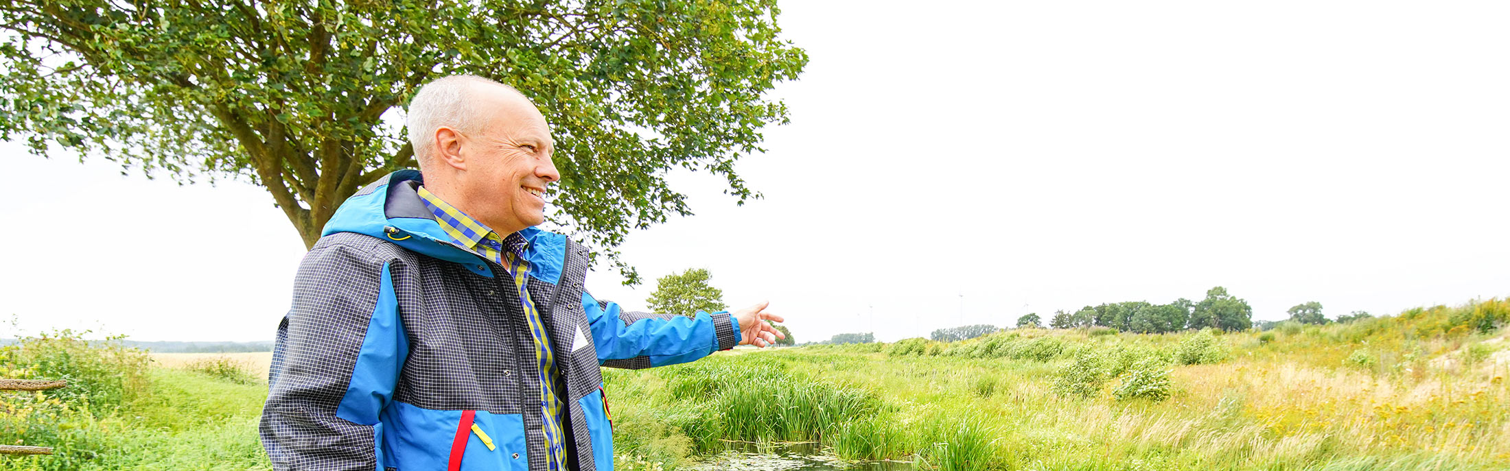 Dietmar Fischer zeigt über eine weite Wiesenlandschaft
